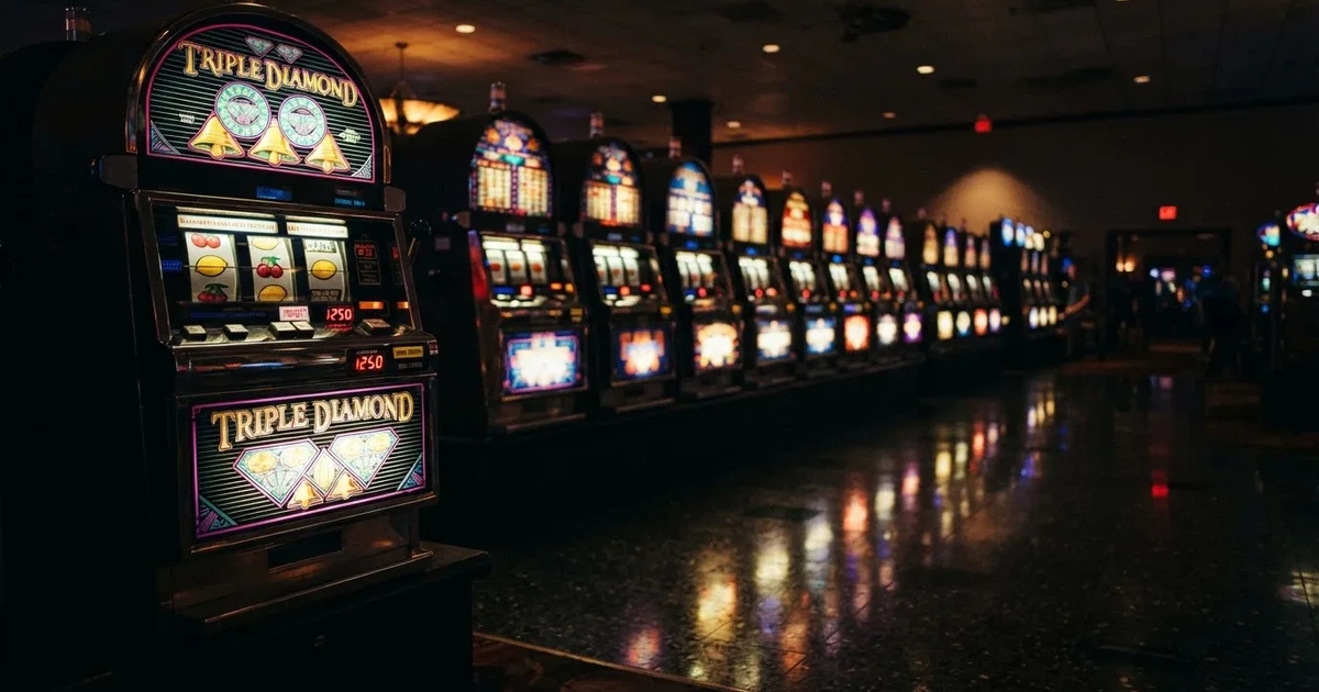 Pelikaappien rivi hämärässä hallissa, jokaisen rullat hohtavat eri väreillä ja lattia heijastaa — kolikkopelit casino pelit